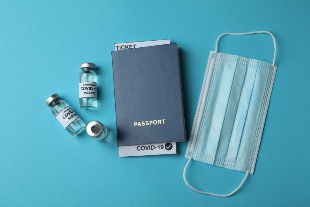 Vials with COVID - 19 vaccine, medical mask and passport on blue background